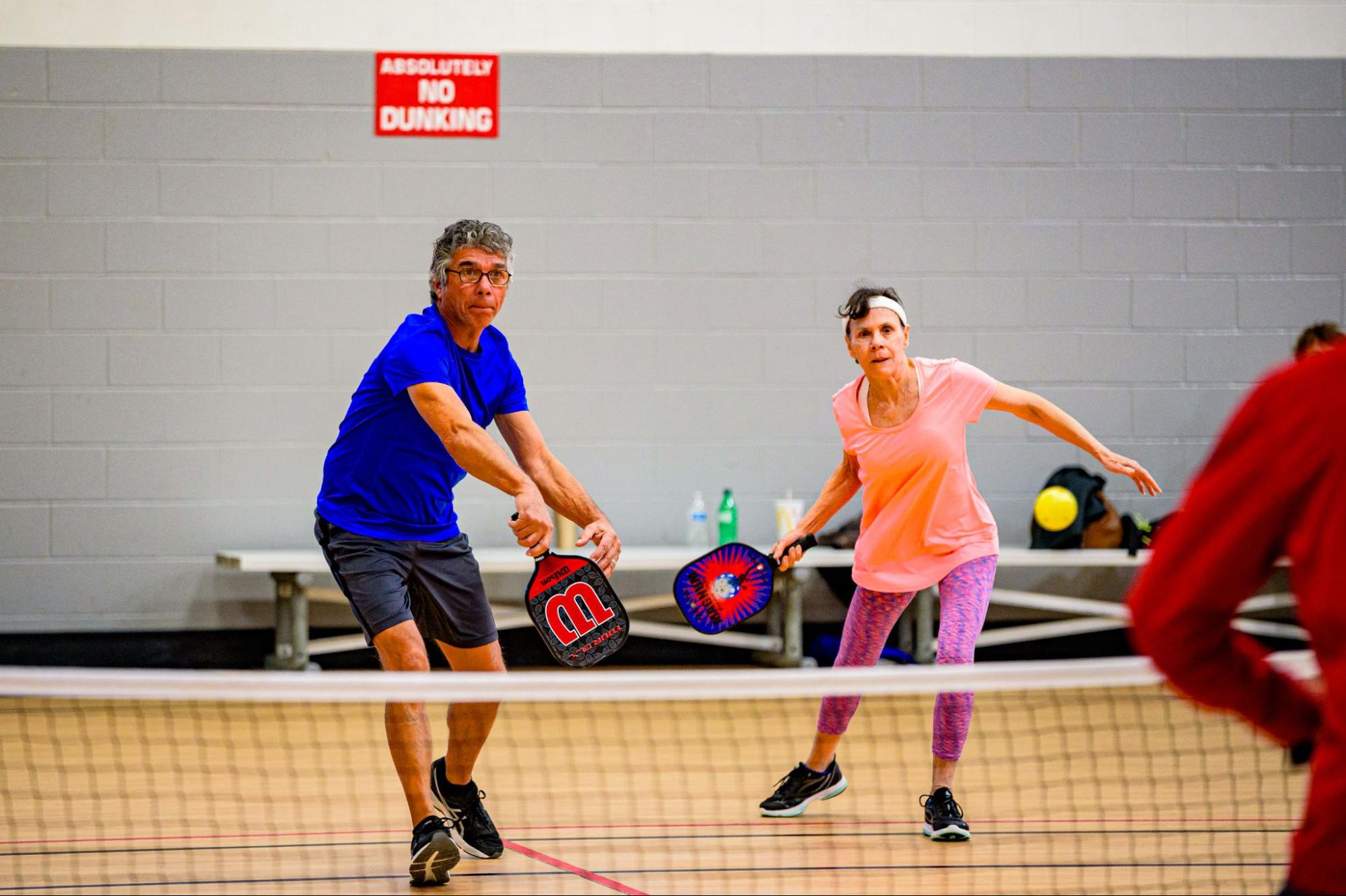 adult man and woman playing pickleball indoors